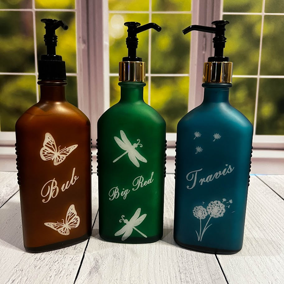 Three decorative bottles with pump tops, each featuring a different design and name, on a wooden surface.