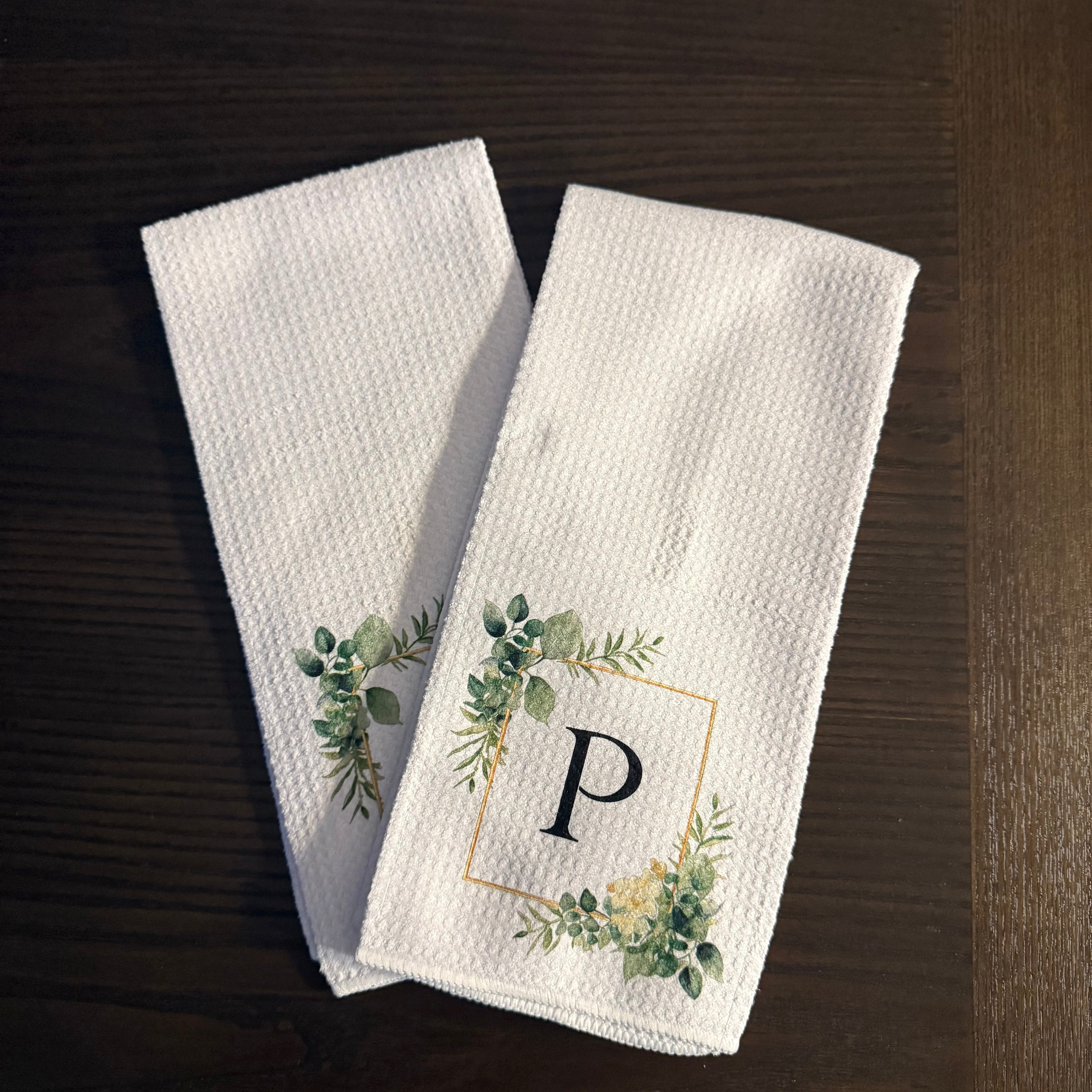 Two white towels with green leaf designs on a dark surface